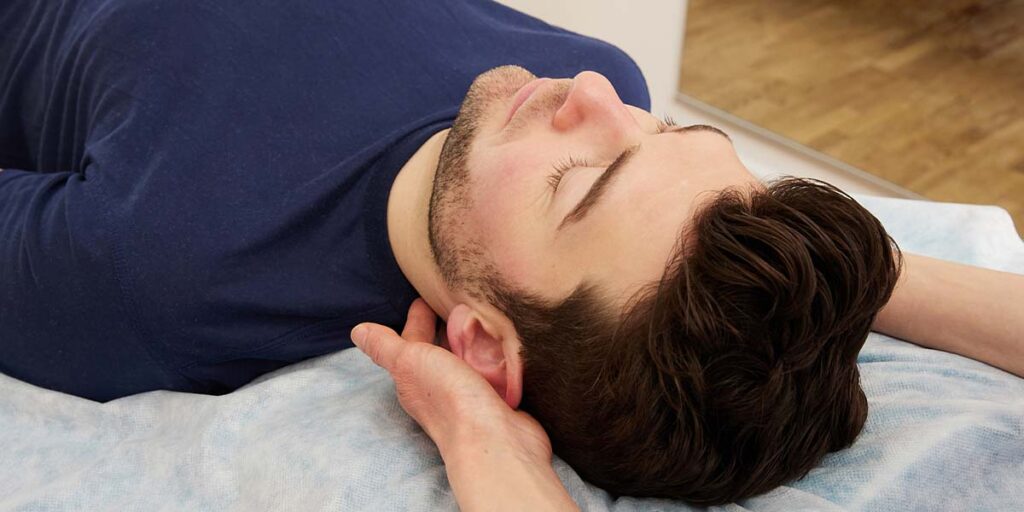 Osteopathin hält den Hinterkopf eines Patienten, begleitende Behandlung bei Migräne